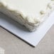 A close up of a white frosted cake on a white Enjay 1/2 sheet cake board.