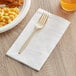 A plastic fork on a white 3-ply dinner napkin with macaroni and cheese.