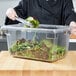 A woman using a Carlisle food storage box to hold salad on a counter.