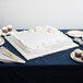 A white cake on a silver square cake drum on a table.
