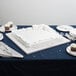 An Enjay white square cake drum under a frosted white cake on a table.