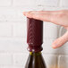 A hand using a Franmara burgundy wine saver vacuum pump bottle stopper to seal a bottle of wine.