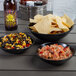 A black melamine serving bowl filled with food on a table with other bowls of food and a bottle of beer.