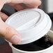 A hand using a Solo white plastic lid to cover a coffee cup.