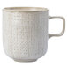A white Oneida Knit porcelain mug with a speckled tan design and handle.