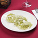 A Tuxton Venice oval china platter with green ravioli with cheese and parmesan on it on a table.