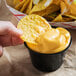 A person dipping a chip into a cup of Gehl's Sharp Cheddar Cheese Sauce.