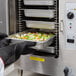 A person in a school kitchen putting food into a Cleveland SteamChef electric steamer.