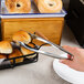 A person using American Metalcraft stainless steel tongs to serve a donut