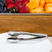Stainless steel tongs serving fruit on a plate.