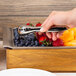 A hand using American Metalcraft stainless steel tongs to serve fruit on a table.