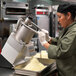 A woman in a chef's uniform using a Hobart continuous feed food processor to grind food.