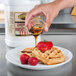 A person pouring Golden Barrel sugar free syrup onto waffles and strawberries.