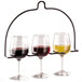 A Vollrath metal stand holding three wine glasses on a table in a cocktail bar.