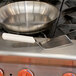 A Dexter-Russell white plastic handled solid turner in a pan on a stove.