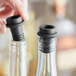 A hand using a Franmara black VinoVac wine stopper to seal a bottle of wine.