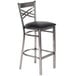 A Lancaster Table & Seating clear coat finish cross back bar stool with a black vinyl seat pad.
