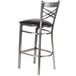 A Lancaster Table & Seating clear coat finish cross back bar stool with a black vinyl padded seat.