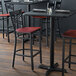 A Lancaster Table & Seating black cross back bar stool with a mahogany seat at a table in a restaurant.