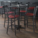 Lancaster Table & Seating black finish cross back bar stools with mahogany wood seats at a table in a restaurant