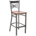 A Lancaster Table & Seating metal cross back bar stool with a cherry wood seat.