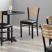 A Lancaster Table & Seating black bistro chair with natural wood back and black vinyl seat detached.