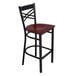 A Lancaster Table & Seating black metal cross back bar stool with a mahogany wood seat.