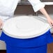 A person holding a white Continental round trash can lid over a blue trash can.