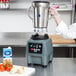 A person wearing gloves uses a Waring stainless steel food blender with a black and grey dial.