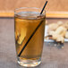 A Libbey highball glass of brown liquid with a straw.