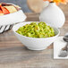 A bright white Acopa porcelain bowl filled with guacamole on a table with a bowl of chips.