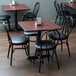 A Lancaster Table & Seating black cast iron table base with a table and black chairs in a restaurant.