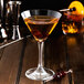 A martini glass of liquid with Fabbri Amarena cherries on a wooden surface.