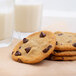 A stack of chocolate chip cookies with a glass of milk on a table.