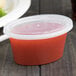 A Newspring clear plastic oval souffle container with a clear lid filled with red liquid.