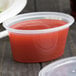 A Newspring clear oval souffle container with a clear lid containing red liquid.