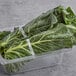 A plastic container of bunched collard greens with green leaves inside.