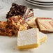 A white plate with a variety of unsliced Sweet Street dessert bars on a table.