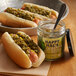 A hot dog with Cortazzo jalapeno relish and mustard next to a jar of Cortazzo jalapeno relish.