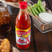 A close up of a bottle of Texas Pete Original Hot Sauce on a table with a basket of fried chicken.
