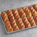 A tray of sliced Bavarian pretzel hot dog rolls on a baking sheet.