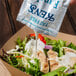 A person pouring a Ken's Fat Free Ranch dressing packet onto a salad.