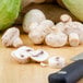 A close up of a White Mushroom on a white surface with a knife.