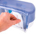 A hand holding a blue and white San Jamar Versatwin double roll toilet paper dispenser.