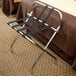 A black metal Lancaster Table & Seating folding luggage rack with guard straps.