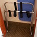 A Lancaster Table & Seating chrome folding luggage rack with straps attached to it.