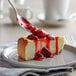 A spoon with J. Hungerford Smith Sliced Strawberry Topping on a slice of cheesecake.
