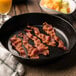 Sliced Kunzler bacon cooking in a skillet with a pan of fruit.