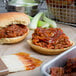 A barbecue sandwich with Sweet Baby Ray's Sweet Red Chili Pepper Wing Sauce on a counter.