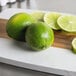 A cutting board with limes on it.